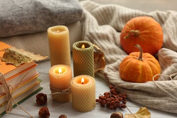 Burning candles, books, sweaters and autumn decor on grey wooden table