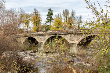 Old stone bridge over the river. Autumn perspective, details from the streets of Debnevo, village in Northern Bulgaria