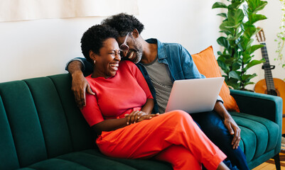 Happy couple laughing and relaxing on the sofa with a laptop