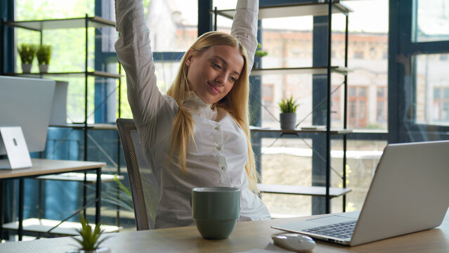 Caucasian businesswoman business manager use laptop check email overwork computer at desk relaxed girl stretch hands woman have coffee break in office relax for tea drink hot beverage free time pause