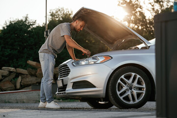Beautiful sunlight. Hood is opened, guy is repairing the automobile. Man is with his car outdoors