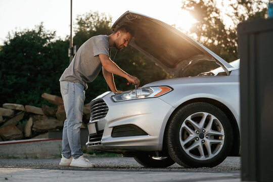 Beautiful sunlight. Hood is opened, guy is repairing the automobile. Man is with his car outdoors