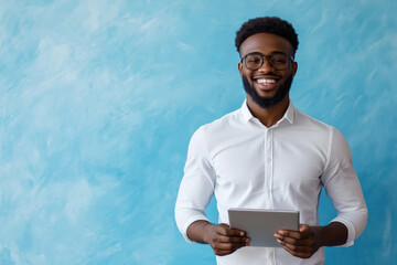 Young Black businessman smiling confidently in an office, holding a touchpad, standing against a blue background.
