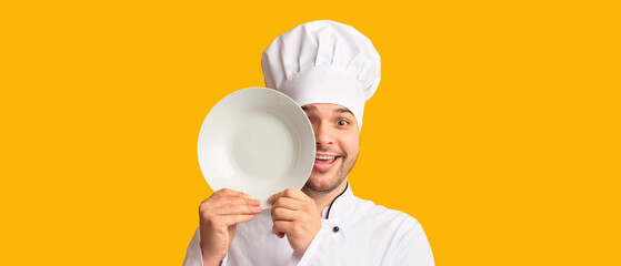 Funny Cook Man Covering Eye With Plate Looking At Camera Standing Over Yellow Studio Background....