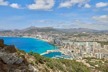 Fototapeta premium Breathtaking view from the cliff overlooking the stunning Calpe Bay in Spain with crystal-clear waters, sandy beaches, and majestic rock formations under a vibrant blue sky. Panoramic seascape of the