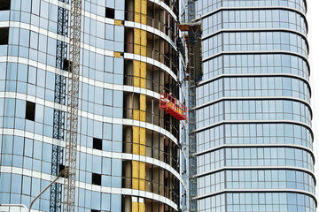 Building under construction with suspended platform for glass facade panel installation, insulation...