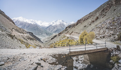 Dusty road of the Pamir Highway in the valley of the Tien Shan Mountains in Tajikistan in the Pamirs and a mountain stream below flows in the valley