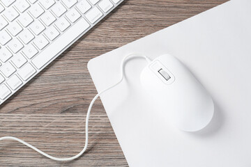 Computer mouse with mousepad and keyboard on wooden desk, top view