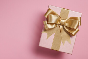 Gift box with bow on dusty pink background, top view