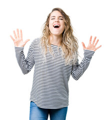 Beautiful young blonde woman wearing stripes sweater over isolated background celebrating mad and...