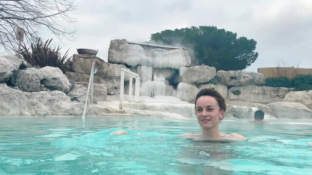 Smiling woman in thermal hot water pool under the open air, relaxing day in natural geothermal baths with sulphur mud on the bottom and healing vapours, therapy for immune system and wellness