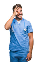Fototapeta premium Young handsome doctor surgeon man over isolated background doing ok gesture with hand smiling, eye looking through fingers with happy face.