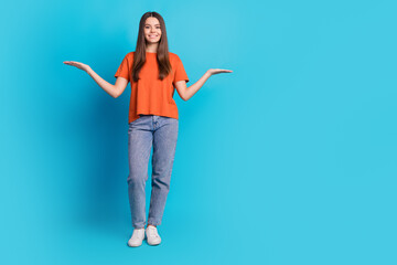 Full body photo of attractive teen woman compare hold empty space dressed stylish orange clothes isolated on blue color background