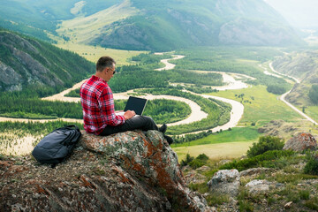 man traveler blogger work remote on laptop while enjoying summer nature landscape