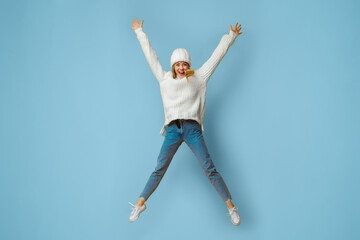 Happy blonde woman in winter hat jumping in the air like a star over yellow studio background