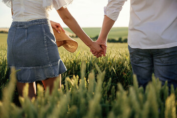 Close up view, holding each other's hands. Lovely couple are on the green agricultural field together