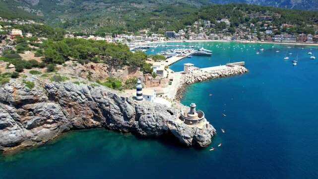Breathtaking aerial 4K drone view of Port de Soller marina and lighthouse. Scenic Mediterranean harbor with luxury yachts at the foot of Tramuntana mountains, Mallorca, Spain.