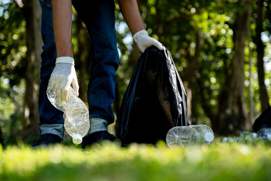 Hand holding plastic bottle waste, picking up trash and putting it in the black garbage bag at the Park on Environmental Earth day