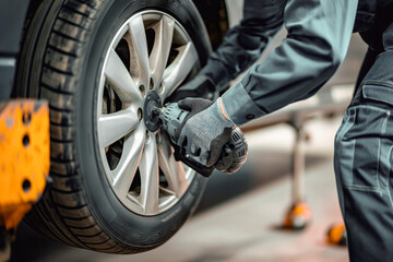 Fototapeta premium Mechanic using a power tool to fasten a wheel in a workshop, wearing gloves and workwear, focusing on the vehicle's maintenance.