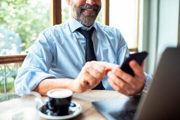 Smiling businessman using smartphone with laptop in a cafe