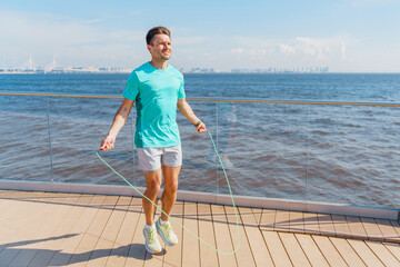 A man jumps rope on a sunny boardwalk by the sea, enjoying a bright day and waterfront view.