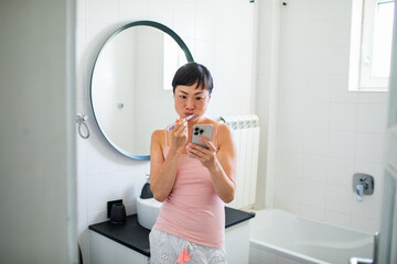 Asian woman brushing teeth and using smartphone in the bathroom