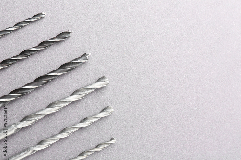 Poster many different drill bits on light grey table, top view. space for text