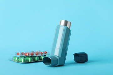 Inhaler and pills on light blue background, closeup. Asthma treatment
