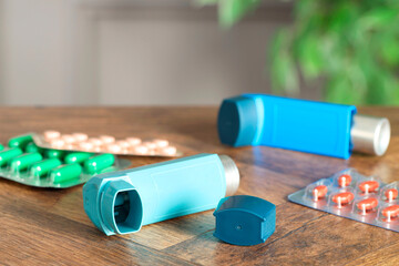 Inhalers and pills on wooden table indoors, closeup. Asthma treatment