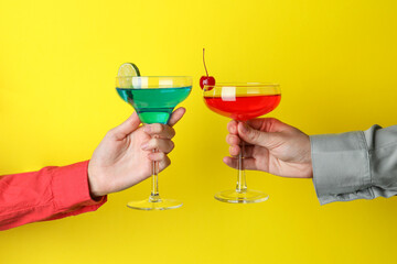 Friends with glasses of refreshing cocktails on yellow background, closeup