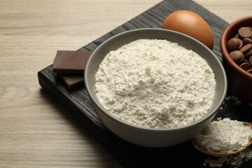 Flour in bowl, egg and chocolate for making dough on wooden table, closeup