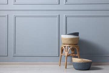 Stylish stool and many wicker baskets near light grey wall indoors, space for text