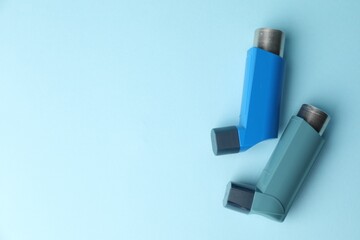 Asthma inhalers on light blue background, top view. Space for text