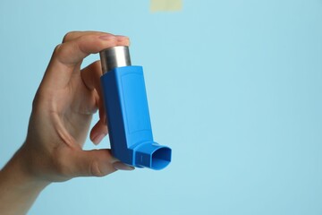 Woman holding asthma inhaler on light blue background, closeup. Space for text