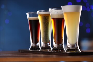 Glasses with different types of beer on wooden table against blue background, closeup. Space for text