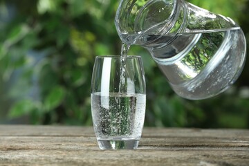 Pouring soda water in glass at wooden table outdoors