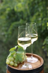 Tasty wine in glasses and grapes on wooden barrel outdoors