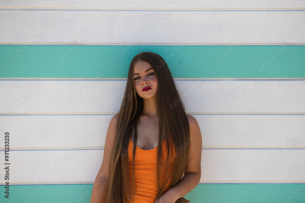 Wall mural beautiful young woman with long hair in an orange dress, on the white and turquoise striped wooden w