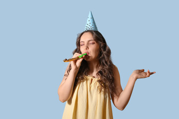 Young woman in birthday hat and with party blower on light blue background