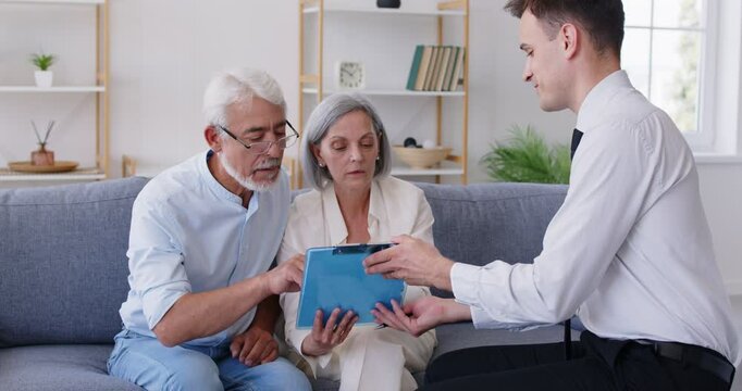A financial advisor and an elderly couple are discussing a document in the living room. Senior couple meeting with investment consultant. Concept of will or life insurance on home, wealth management