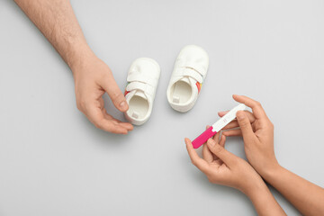Hands of loving young couple with pregnancy test and baby booties on grey background