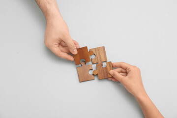 Hands of loving young couple with wooden puzzle pieces on grey background