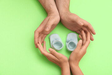 Hands of loving young couple with baby booties on green background
