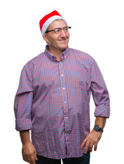 Handsome senior man wearing christmas hat over isolated background looking away to side with smile on face, natural expression. Laughing confident.