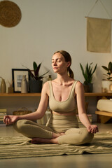 Young modern woman with closed eyes and crossed legs sitting on the floor in pose of lotus and practicing meditation exercises