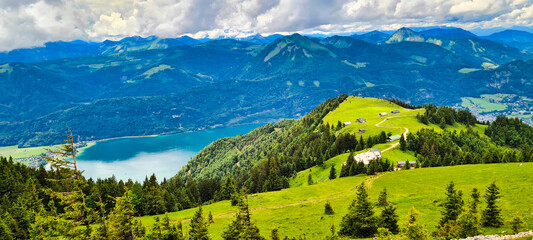 A breathtaking view from the Schafberg in Austria, showcasing lush green meadows, mountain ridges, and the stunning Wolfgangsee in the distance. The perfect spot for hiking and soaking in the panorami