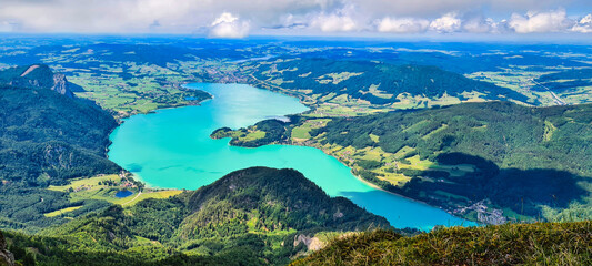 A stunning view from Schafberg, Austria, showcasing the vibrant turquoise waters of Wolfgangsee surrounded by lush green valleys and mountains. This breathtaking alpine scenery is a popular destinatio