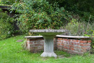 Stone table and brick bench among herbs, native plants and wild rose hip shrubs in an eco-friendly natural country garden, idyllic seating place, copy space