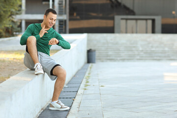 Sporty young man checking pulse after training outdoors