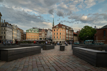 Fototapeta premium A bustling scene unfolds in Riga's iconic Dome Square, featuring historic buildings, a charming statue, and locals enjoying the lively atmosphere.